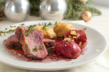 Festive holiday dinner, roasted duck slices with fig, mashed parsnip and red wine sauce on a white plate, Christmas decoration in the background, close up shot, selected focu