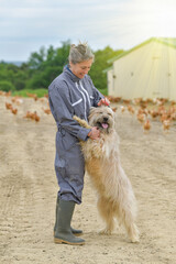 Portrait of a farmer petting her dog and standing in the middle of her chicken farm