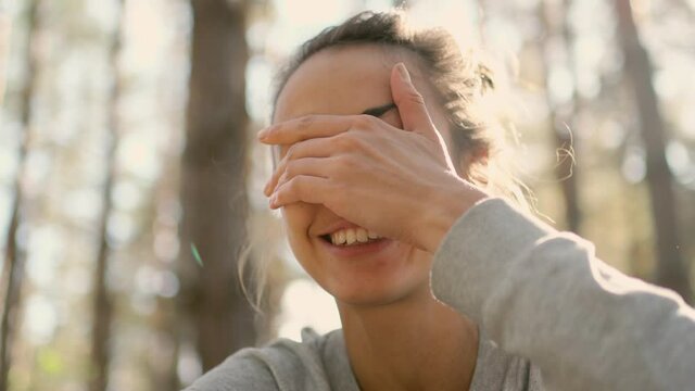 close up portrait of cheerful young woman laughs and smiling looking straight at camera. POV, girl spending time with some one in woods joking and getting fun