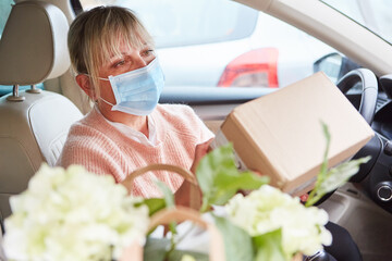 Frau mit Mundschutz prüft Paket im Innenraum ihres Autos
