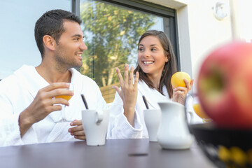Happy young couple in bathrobes having breakfast outdoors