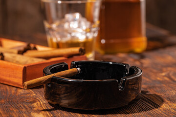 Glass of whisky and lighted cigar in an ash tray