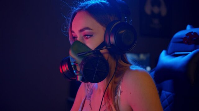 Young gamer woman in respirator sitting by the PC in corduroy top and playing a game