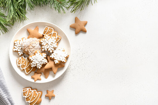 Christmas handmade glazed cookies in plate decorated fir branches on white background. View from above. Flat lay.