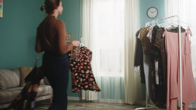 Girl enters a spacious room and hangs women's clothes on a hanger. She runs her hand over the dresses