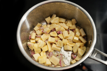 Cooking parsnip and red onions in a stainless steel saucepan on the black stove for a healthy vegetarian meal