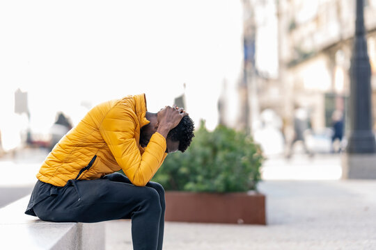Profile of a sad African man complaining sitting on a bench alone in a city