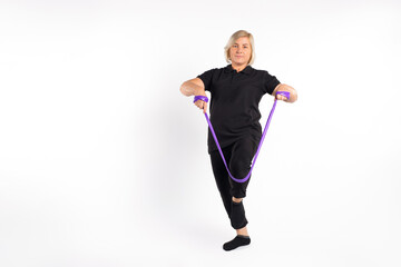 Senior woman stretches elastic band with her leg, on white empty space. Healthy, pandemic concept.