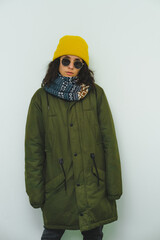 Beauty girl in trendy urban street outfit. Stylish posing. Green warm down jacket, scarf, sunglasses and yellow beanie.