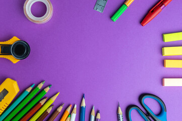Workspace with office supplies. Scissors, tape, pens, pencils and stickers on a purple background