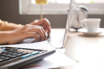 Calculator on office desk with blurry hand writing on laptop on the background