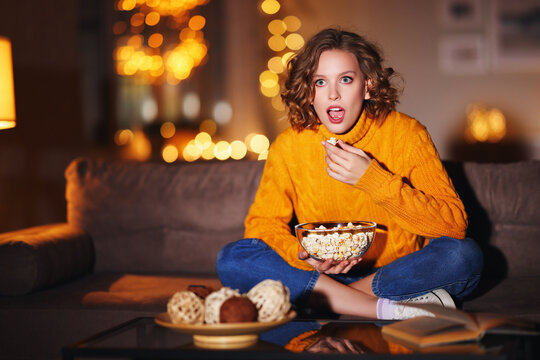 Young female eating popcorn and watching interesting movie