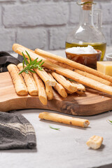 Traditional italian breadsticks grissini with rosemary, parmesan cheese, olive oil, garlic and salt on a gray background.