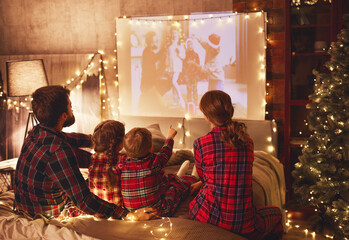 family mother father and children watching projector, film, movies with popcorn in   christmas evening   at home.