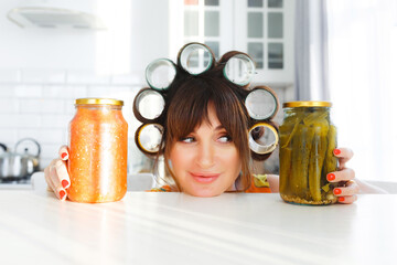 attractive housewife with curlers holds two glass jars of food in a bright kitchen