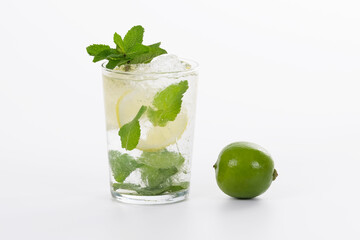 view of a refreshing glass of mojito cocktail next to a fresh lime on a light background