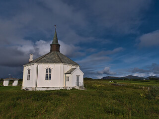 Fototapeta na wymiar Historic wooden church constructed in octagonal style with white painted facade between green meadows near village Dverberg on Andøya island, Vesterålen,Norway on sunny day in late summer with clouds.