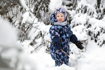 Fototapeta na wymiar Cheerful smiling toddler girl wearing winter clothes having fun outside in snowy forest. Christmas and new year holidays