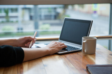 Hands using laptop and notebook with cup of tea on wooden table in cafe