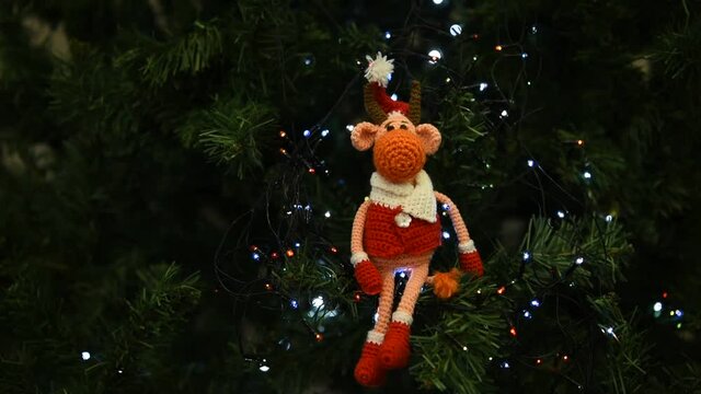 knitted red bull toy sitting on Christmas tree with bokeh lights in the dark 