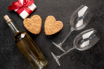 Fototapeta na wymiar A festive dinner for two on Valentine's Day. Heart shaped cakes and white wine bottle with glasses, gift on stone background