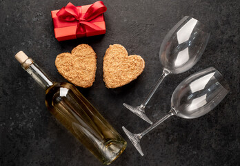 Fototapeta na wymiar A festive dinner for two on Valentine's Day. Heart shaped cakes and white wine bottle with glasses, gift on stone background