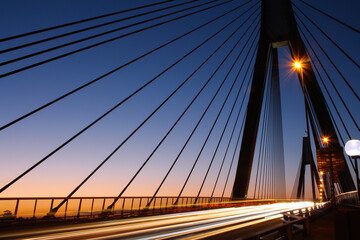 Fototapeta na wymiar Cable bridge at sunset. Long exposure, vehicle headlight trails at a cable bridge at sunset.