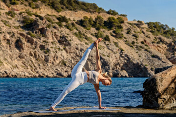 Young woman doing side plank split by the sea.