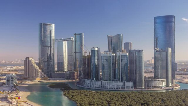 Buildings on Al Reem island in Abu Dhabi timelapse from above. Aerial citiscape of Al Reem Island at evening, showing the reflection of buildings in the water and long shadows.