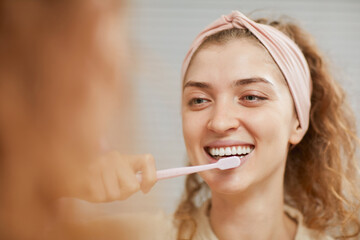 Young woman smiling at camera while cleaning her teeth in the morning