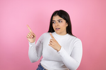 Young beautiful woman over isolated pink background surprised and pointing her fingers side