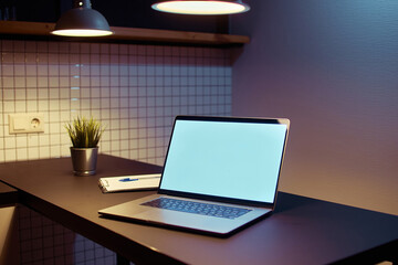 Fototapeta premium Workspace for remote online work at a laptop with empty white screen mockup in a modern loft interior