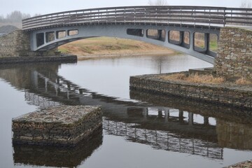 Fototapeta premium Modern metal pedestrian bridge across the river on a stone foundation.