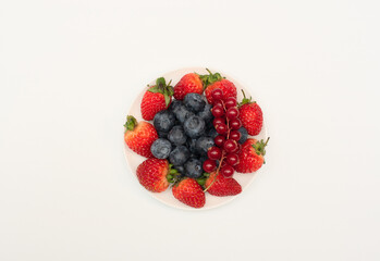 Various fresh summer berries: strawberries, currant, blueberries on white plate on white background. Summer time concept. Vitamins, healthy eating, harvest. Selective focus. Flat lay style.