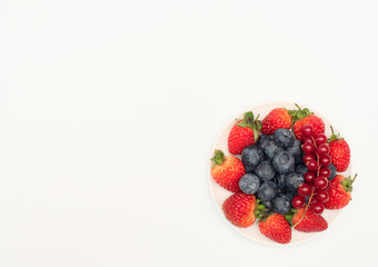 Various fresh summer berries: strawberries, currant, blueberries on white plate on white background. Summer time concept. Vitamins, healthy eating, harvest. Selective focus. Flat lay style.