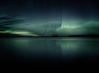 Northern lights dancing over calm lake in Farnebofjarden national park in north of Sweden.