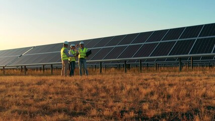 Three solar energy specialists having a discussion on a solar farm. Professional engineers discuss innovative project.