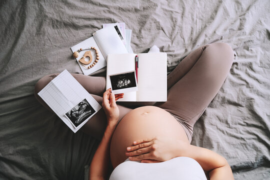 Pregnant woman holding ultrasound image looking at notebook and medical test reports.