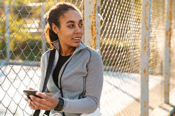 Joyful african american sportswoman using mobile phone outdoors