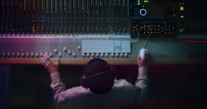 Cinematic top view of professional male sound producer with headphones is recording a new song with young singer in a music studio with colorful lights on a background.