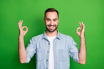Portrait of optimistic funny man wear blue shirt show okey signs isolated on green color background