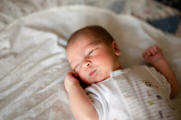 Newborn baby for the first time at home, lying in a blanket on the bed, smiling, yawning, pulling pens, falling asleep, baby's morning, baby products concept.