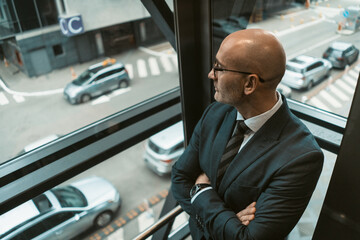 Top angle view. Contemplative bald businessman in suit and glasses looking away in the window or...