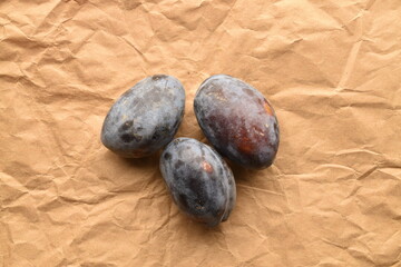 Ripe dark purple plums, close-up, on brown paper.