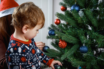 Beautiful girl with her son decorate the Christmas tree in the house. Happy family.