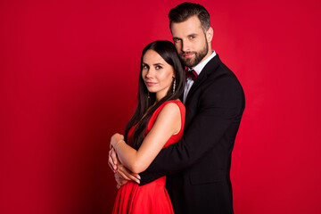 Profile portrait of two nice positive persons guy hugs lady from behind enjoy each other isolated on red color background