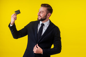 Portrait of handsome young businessman holding credit card over yellow background