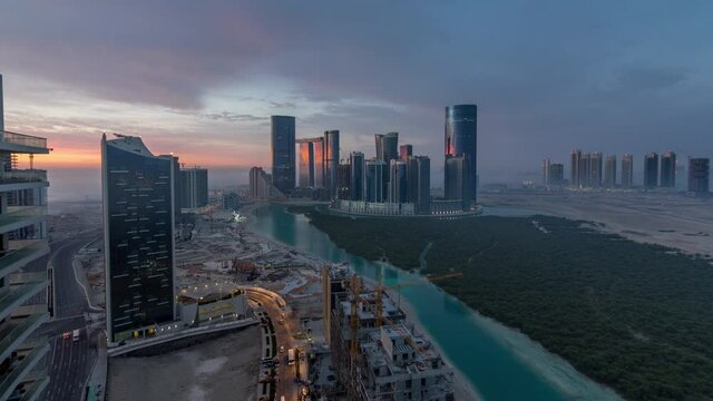 Skyscrapers on Al Reem in Abu Dhabi timelapse during sunrise from above. Aerial citiscape from Al Reem Island at morning with fog. Sun reflected on glass surface