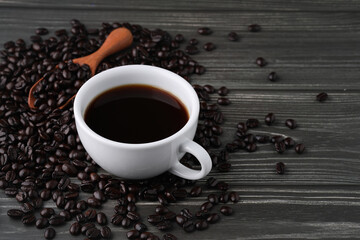White cup of black coffee with beans and wooden spoon on dark vintage wooden table. Freshness breakfast Americarno with copy space for your advertising content