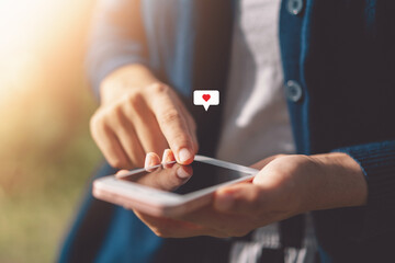 Close up woman hand hold using smart phone with heart icon at outdoor park street background. Copy...